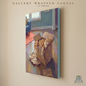 May include: A gallery wrapped canvas with a 1.5 inch depth featuring a painting of an orange tabby cat resting inside a brown cardboard box on a wooden floor. The scene includes a blue chair and a red rug in the background. The text reads GALLERY WRAPPED CANVAS 1.5" DEPTH.