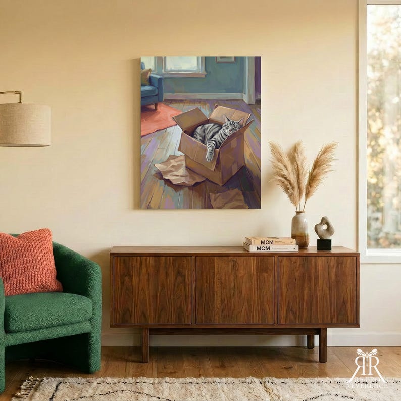 May include: A wall art print depicting a grey and white tabby cat resting inside a brown cardboard box on a wooden floor. The painting features a blue chair in the background, a warm color palette, and visible brushstrokes throughout the composition.