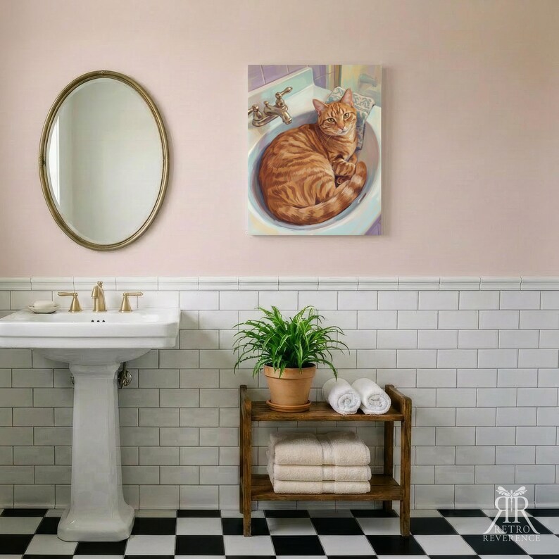 May include: A rectangular wall art print featuring an orange tabby cat curled inside a white bathroom sink. The artwork is displayed in a bathroom with a pedestal sink, an oval mirror, a green potted plant, and stacked white towels.