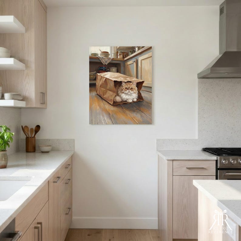 May include: A framed wall art print depicting a fluffy ginger cat sitting inside a brown paper grocery bag on a wooden floor. The cat has long fur and a serious expression. The artwork is displayed on a white wall in a kitchen setting.