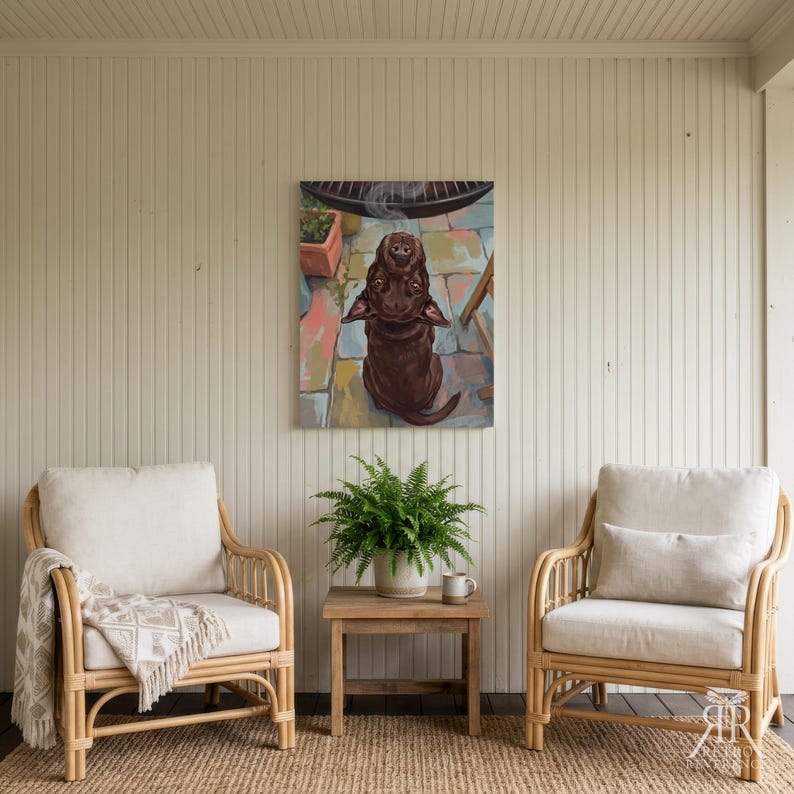 May include: A rectangular wall art print featuring a brown dog sitting on a colorful stone patio, looking upward with a small wisp of steam rising above its head. The artwork is displayed on a vertical white paneled wall between two rattan chairs.