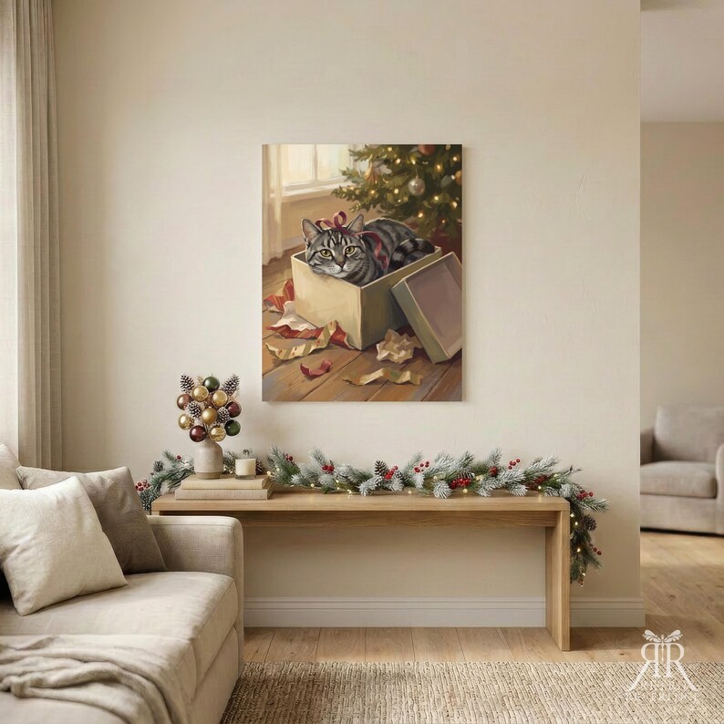 May include: A square wall art print featuring a grey tabby cat sitting inside a cardboard gift box with a red ribbon on its head, positioned on a wooden floor near a Christmas tree with scattered wrapping paper and a detached box lid.
