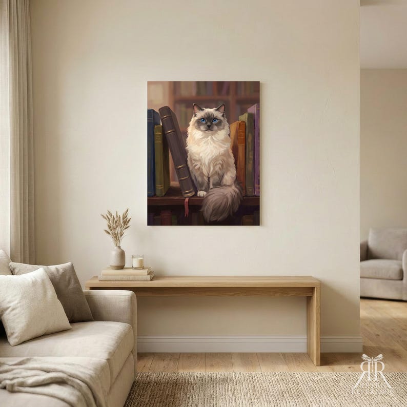 May include: A rectangular wall art print featuring a fluffy, cream-colored cat with dark brown points and bright blue eyes sitting on a wooden shelf. The cat is positioned between several upright, colorful hardcover books in a library setting.