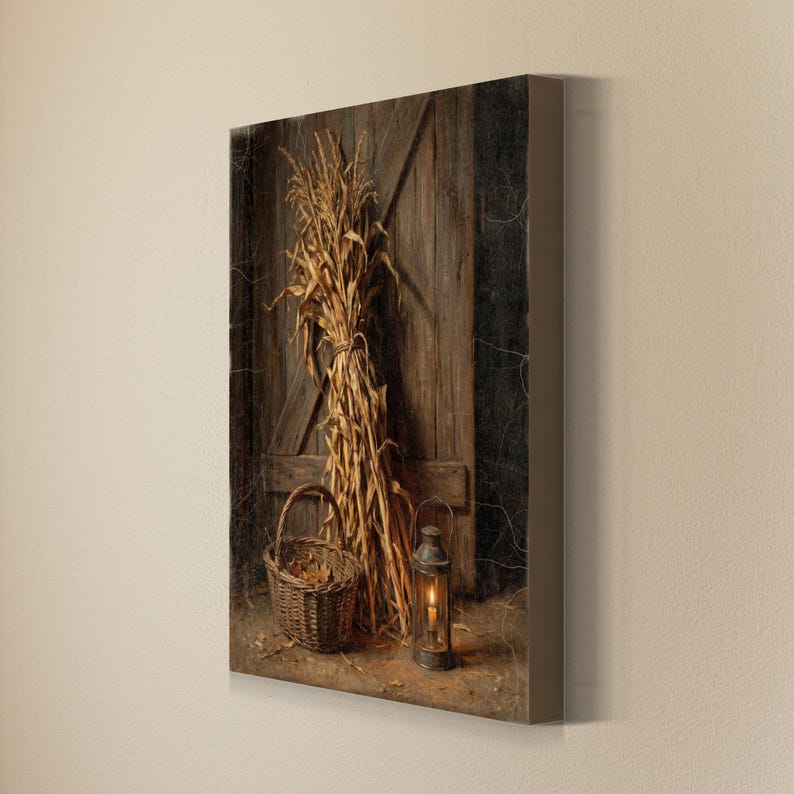 May include: A rectangular canvas print featuring a bundle of dried corn stalks leaning against a weathered brown wooden door. A woven wicker basket sits to the left, and a metal lantern with a glowing candle is positioned on the ground.