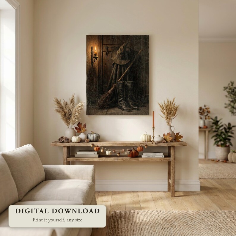 Moody vintage style Halloween art of a witch’s hat, broom and boots, hung on a wall in a cozy living room decorated for fall, shown as a digital file you print yourself