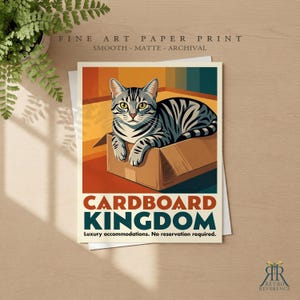 May include: A fine art paper print featuring a gray tabby cat sitting inside a cardboard box. The text reads CARDBOARD KINGDOM, Luxury accommodations. No reservation required. The print is smooth, matte, and archival, with a retro color palette.