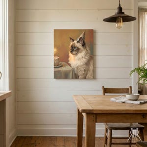 May include: A square wall art print featuring a fluffy, long-haired cat with blue eyes and dark points, wearing a small party hat. The cat sits beside a table with a lit birthday cake. The background is a warm, soft-toned, painterly scene.