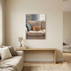 May include: A framed wall art print depicting a small, fluffy, light brown dog curled up asleep on a beige sofa. The painting features soft, painterly brushstrokes with a blue accent pillow on the couch and a window in the background.