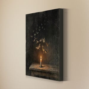 May include: A rectangular canvas wall art print featuring a dark, textured background with a single lit candle resting on a wooden surface. A swarm of moths in shades of brown and cream flies upward from the candle flame into the dark space above.