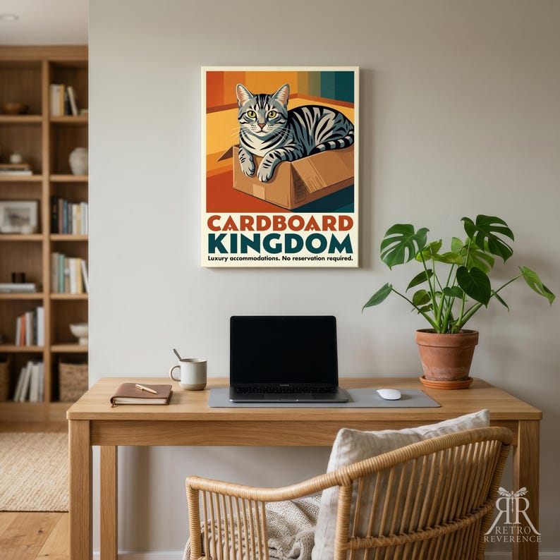 May include: A rectangular wall poster featuring a grey tabby cat sitting inside a brown cardboard box. The text reads CARDBOARD KINGDOM and Luxury accommodations. No reservation required. The background has vertical stripes in orange, yellow, and blue.