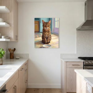 May include: A rectangular wall art print featuring a brown and black spotted tabby cat sitting on a light-colored floor in front of a white bowl. The cat has green eyes and is positioned in a kitchen setting with cabinets and a doorway visible.