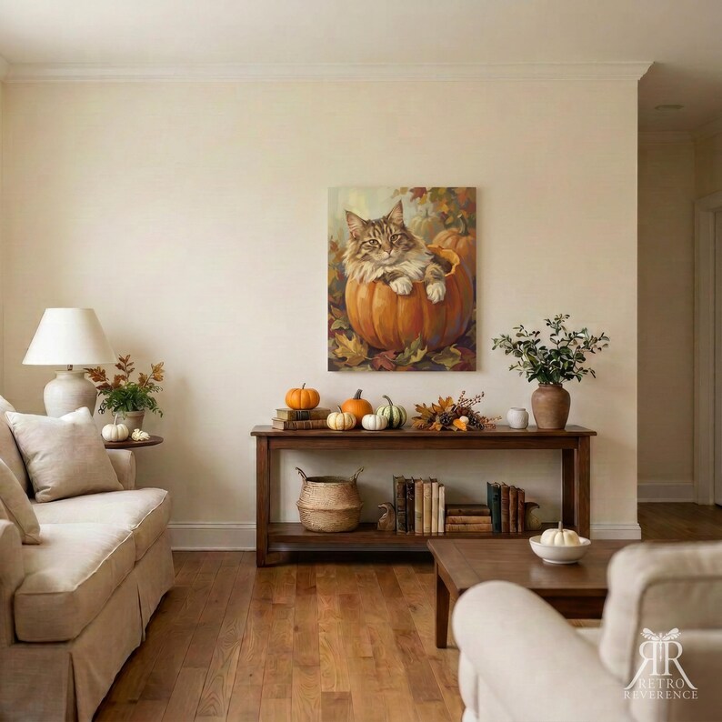 May include: A wall-mounted canvas print depicts a brown tabby cat sitting inside a large orange pumpkin surrounded by autumn leaves. The artwork hangs above a wooden console table holding small pumpkins, books, and a vase with green foliage.