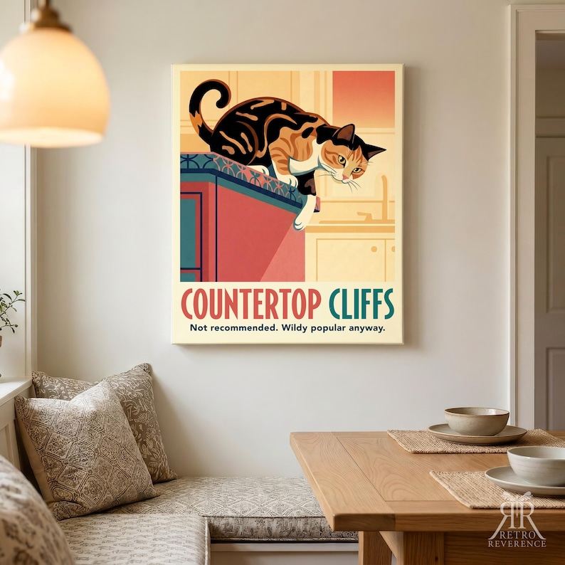 May include: A rectangular wall art print featuring a calico cat perched on a red kitchen counter. The text reads COUNTERTOP CLIFFS and Not recommended. Wildy popular anyway. The illustration uses warm tones of orange, red, and cream colors.