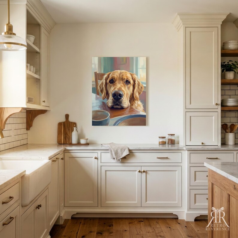 May include: A framed wall art print featuring a golden retriever resting its chin on a wooden table. The dog has light golden fur, dark eyes, and a black nose. The artwork is displayed on a plain wall in a kitchen with white cabinets.