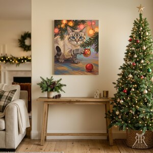 May include: A rectangular wall art print featuring a light-colored tabby cat with blue eyes reaching for a red Christmas ornament hanging from a pine branch, surrounded by warm glowing fairy lights against a soft, colorful background.