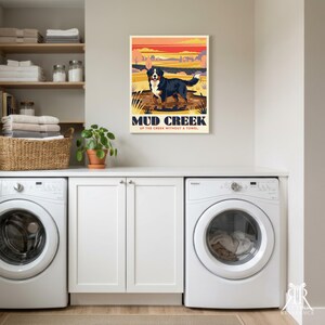 May include: A rectangular wall art print featuring a Bernese Mountain Dog standing in a muddy creek. The text reads MUD CREEK UP THE CREEK WITHOUT A TOWEL. The background shows a stylized landscape with a sunset sky in orange and yellow hues.
