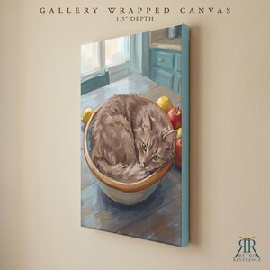 May include: A gallery wrapped canvas with a 1.5 inch depth featuring a painting of a fluffy gray cat curled up inside a ceramic bowl on a wooden table. Beside the bowl are a yellow lemon and a red apple. The text reads GALLERY WRAPPED CANVAS.