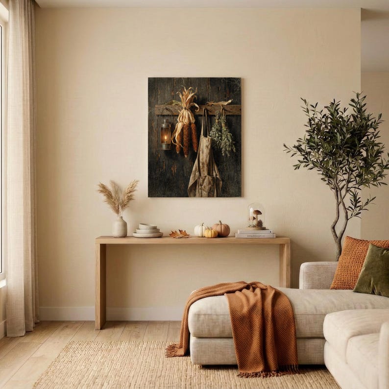 May include: A rectangular wall art print featuring a dark wooden background with a hanging lantern, dried corn husks, a beige apron, and a bundle of green herbs. The artwork is displayed above a long wooden console table in a neutral room.