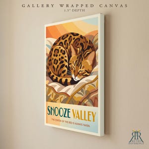 May include: A gallery wrapped canvas with a 3.8 cm depth featuring a graphic illustration of a curled-up leopard-spotted cat. The text reads SNOOZE VALLEY and THE CENTER OF THE BED IS ALWAYS TAKEN. The colour palette includes shades of orange, brown, and cream.