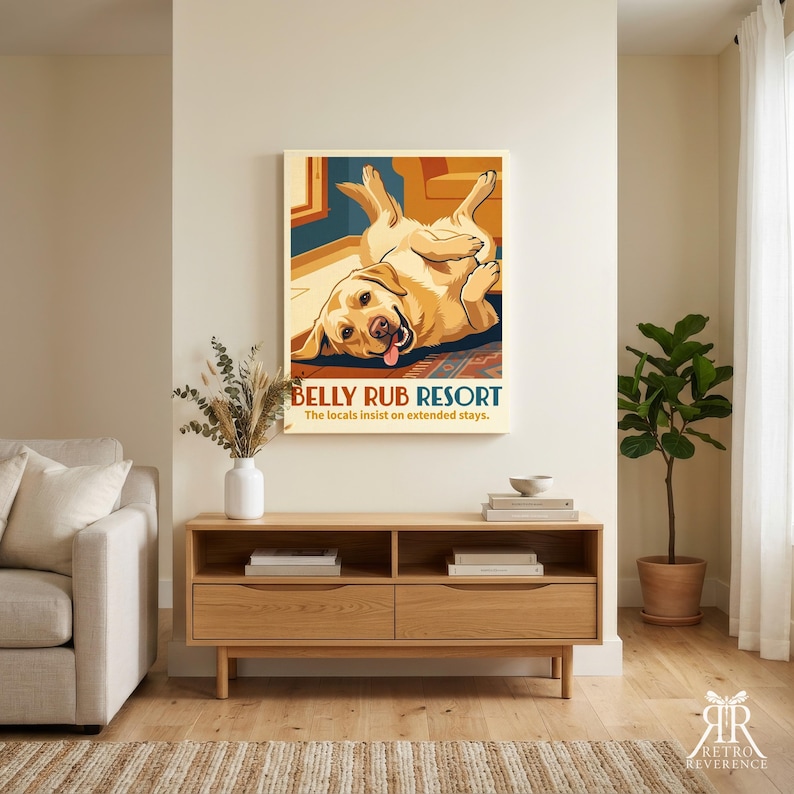 May include: A rectangular wall art print featuring a yellow Labrador retriever lying on its back with its tongue out. The text reads BELLY RUB RESORT and The locals insist on extended stays. The illustration uses warm tones of yellow, orange, and blue.
