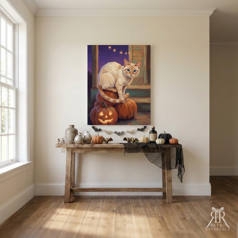 May include: A rectangular wall art print featuring a cream-colored cat with blue eyes sitting atop a stack of orange pumpkins, including a carved jack-o'-lantern, set against a dark purple evening sky with string lights and a porch background.