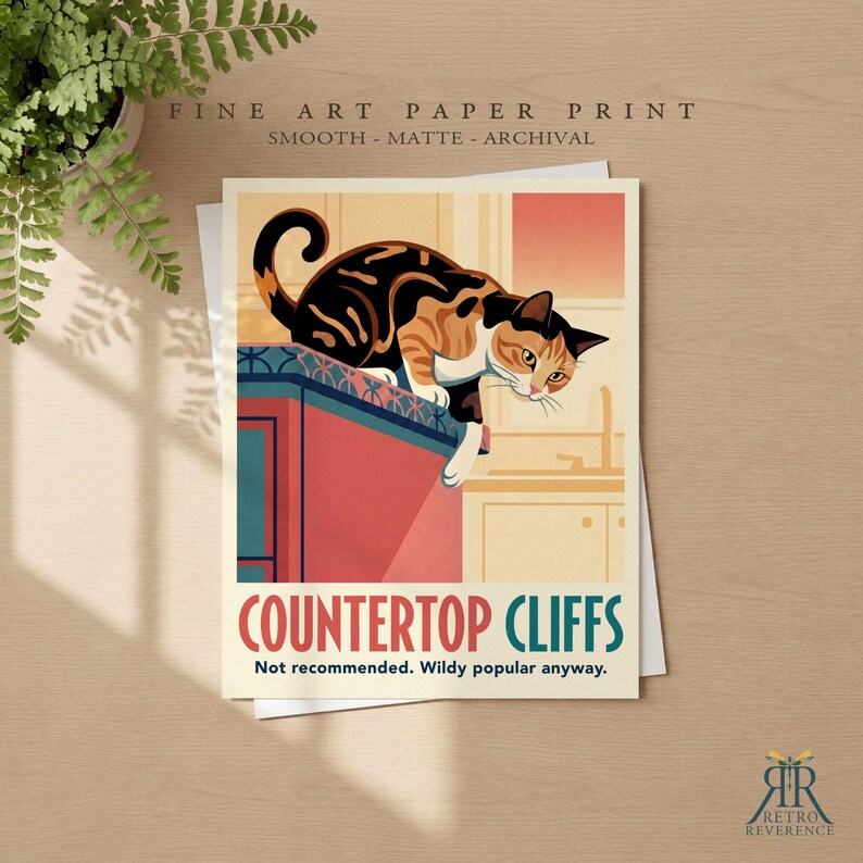 May include: A rectangular art print featuring a calico cat perched on the edge of a red kitchen counter. The text reads "COUNTERTOP CLIFFS" and "Not recommended. Wildy popular anyway." The illustration uses a warm color palette with orange, black, and white tones.