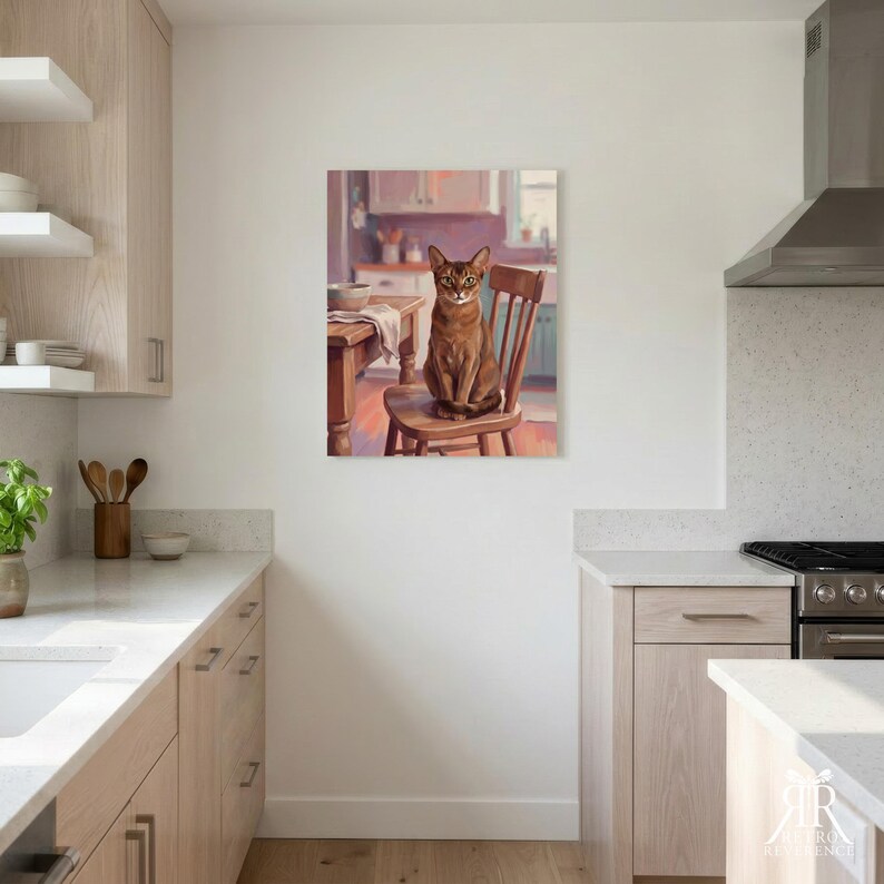 May include: A rectangular wall art print featuring a painting of a brown Abyssinian cat sitting upright on a wooden chair in a kitchen setting. The cat has large ears and green eyes, positioned next to a wooden table with a bowl and cloth.