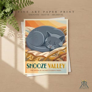 May include: A fine art paper print featuring a graphic illustration of a grey cat curled up on a patterned blanket. The text reads SNOOZE VALLEY and THE CENTER OF THE BED IS ALWAYS TAKEN. The print is smooth, matte, and archival quality.