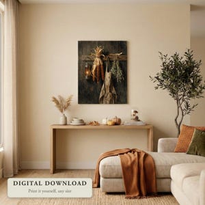 Vintage style still life of dried corn, an apron and herbs hanging by lantern light, hung on a wall in a cozy living room decorated for fall, shown as a digital file you print yourself