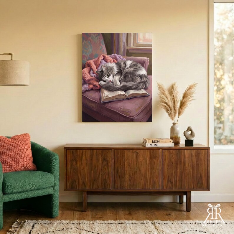 May include: A rectangular wall art print featuring a fluffy gray and white cat curled up asleep on an open book, which rests on a plush purple armchair draped with a soft pink blanket. The artwork displays detailed fur textures and warm lighting.