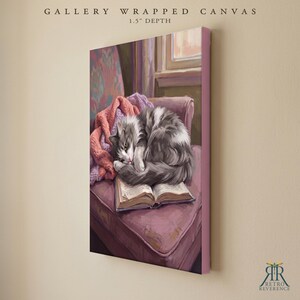 May include: A gallery wrapped canvas with a 1.5 inch depth featuring a painting of a fluffy gray and white cat curled up asleep on an open book. The book rests on a mauve upholstered chair next to a pink knitted blanket, with a window visible in the background.