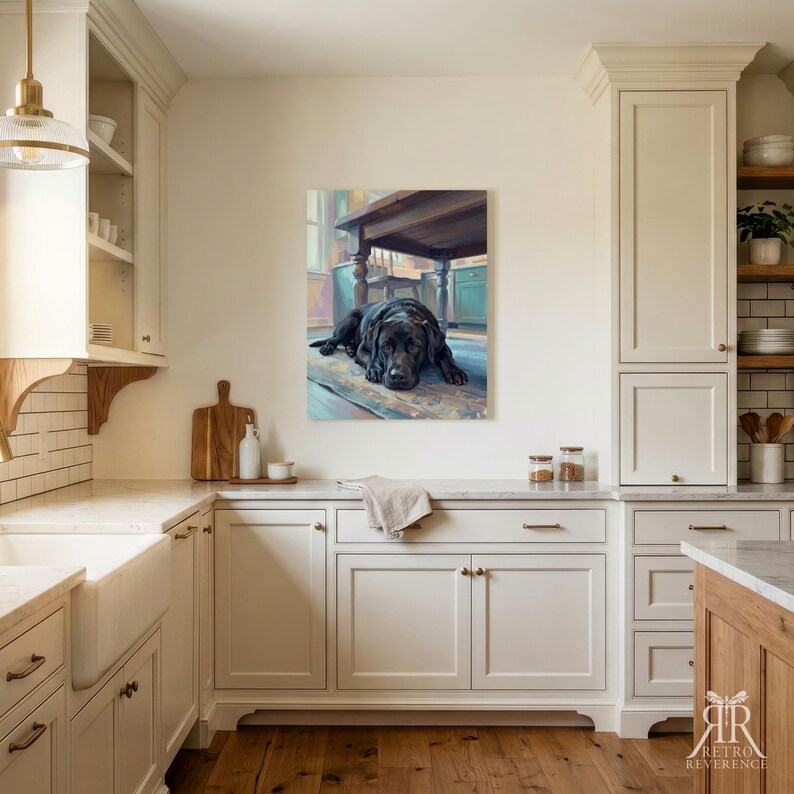 May include: A rectangular wall art print featuring a black Labrador retriever lying on a patterned rug beneath a wooden table. The artwork is displayed on a light-colored wall in a kitchen with white cabinetry, a farmhouse sink, and wooden flooring.