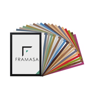 May include: A black rectangular picture frame containing a white mount board with the black text FRAMASA and a geometric logo. Behind the frame, a fan-shaped display of multiple rectangular mount boards in various solid colours and wood grain textures.