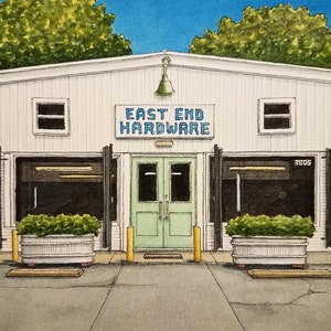 May include: A white building with a blue sign that reads "East End Hardware". The building has two large windows on each side of the entrance and a smaller window above the entrance. There are two large green doors in the center of the building. The building is surrounded by green trees and bushes.