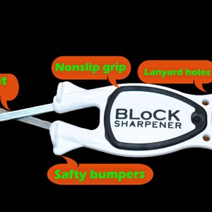May include: White and black Block Sharpener with a non-slip grip, lanyard holes, and safety bumpers. The sharpener has a patent flex and a thumb dip. The text "BLOCK SHARPENER" is printed on the product.