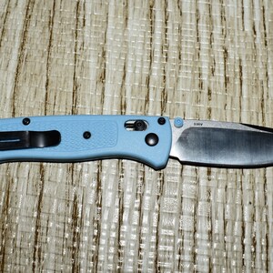 May include: A light blue folding knife with a black pocket clip and hardware. The blade is silver and the handle is a textured light blue. The knife is approximately 8 inches long when open.