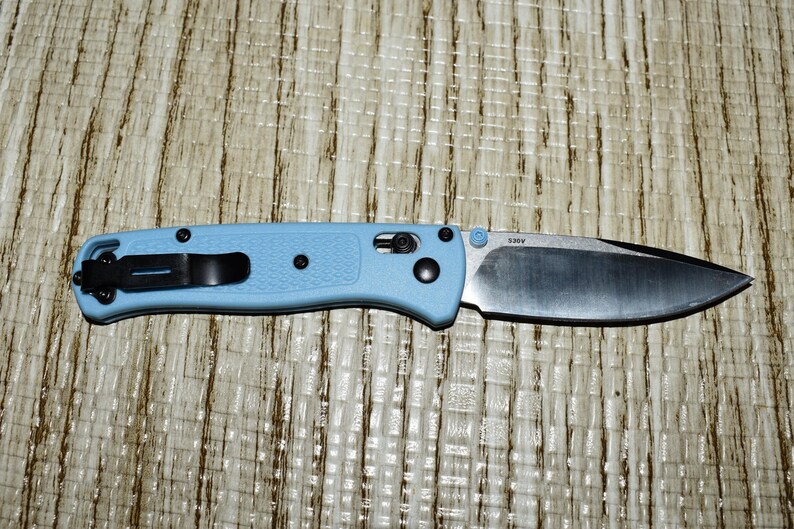 May include: A light blue folding knife with a black pocket clip and hardware. The blade is silver and the handle is a textured light blue. The knife is approximately 8 inches long when open.