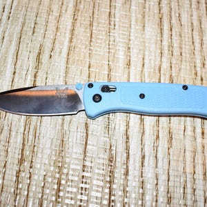 May include: A light blue folding knife with a silver blade. The blade has a logo and the handle has black hardware. The knife is approximately 8 inches long when open.