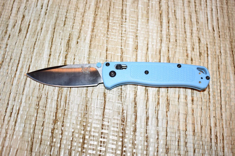 May include: A light blue folding knife with a silver blade. The blade has a logo and the handle has black hardware. The knife is approximately 8 inches long when open.