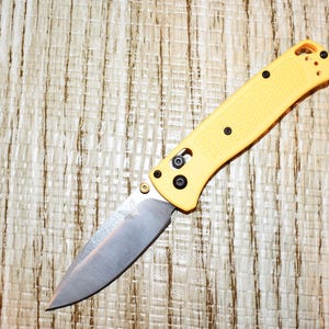 May include: A white ceramic mug with a black handle and the text "But First, Coffee" in a bold, black font. The mug is set against a neutral background, highlighting its simple design.