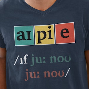 May include: A navy blue t-shirt with a graphic of the word "a-pie" in colorful squares. The text below the graphic reads "/if ju: now ju: now/" in a retro font.