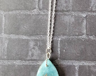May include: A silver chain necklace with a teardrop-shaped pendant. The pendant is made of clear resin with a light blue tint and contains silver glitter and flakes.