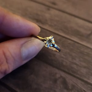 May include: A gold ring with a single, clear, round diamond.