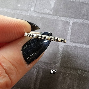 May include: A silver ring with a row of small black beads around the band. The ring is shown on a finger with black nail polish. The text "R7" is visible in the image.