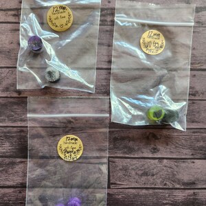 May include: Three small bags containing 12mm handmade resin earrings. The bags are labeled with gold circle stickers that say "12mm handmade with love Purple Gifts". The earrings are in various colors, including purple, black, and green.