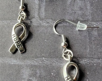 May include: A pair of silver earrings featuring a ribbon charm with the word "HOPE" engraved on it.