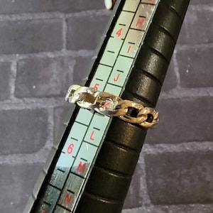May include: A silver and gold chain ring on a ring sizer, showing the ring size is 6.