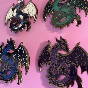 May include: Four metal enamel pins shaped like coiled dragons with outstretched wings. Each dragon features a distinct colour scheme: white and dark blue, green and black, blue and dark blue, and purple and black, all with geometric wing patterns.