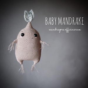 Pode incluir: Boneca Baby Mandrake de crochê em cor bege claro, com olhos pretos e um pequeno sorriso. A boneca tem braços e pernas pequenos com franjas e um top verde folha. O texto "BABY MANDRAKE" e "mandragora officinarum" está escrito à direita.