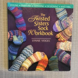 Może przedstawiać: Książka "The Twisted Sisters Sock Workbook" autorstwa Lynne Vogel, z okładką przedstawiającą kolorowe kolekcje dzianych skarpet.